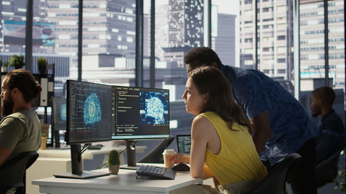 Cybersecurity professionals gathered at a computer in an office with windows overlooking a downtown landscape